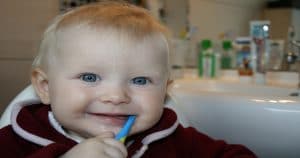 Bebê segurando uma escova de dentes na boca - Saiba aqui como escovar os dentes do bebê