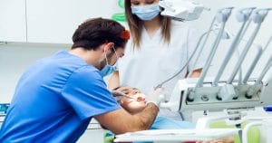 Paciente com a boca aberta sendo atendida por um dentista e sua assistente